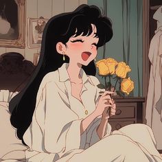 a woman with long black hair sitting on a bed holding a yellow rose in her hand