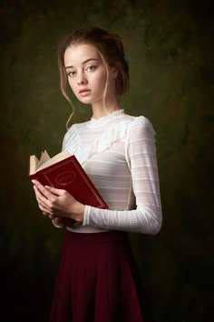 a woman in a white top is holding a red book and looking at the camera