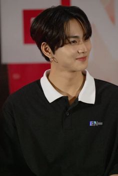 the young man is wearing a black shirt and white collared shirt with his hands on his hips