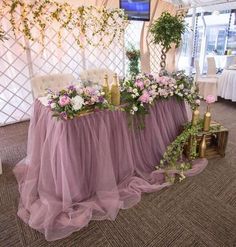 the table is covered in purple tulle and has flowers on it, along with greenery