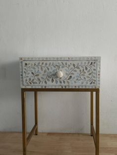 a white and gold painted wooden table with drawers on one side, in front of a wall