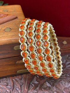 This unique and sophisticated Reverse Polki Sonia bangle is intricately crafted with an orange Polki center and stunning Monalisa stone detailing. Its intricate pearl lining provides unparalleled elegance that will sure to make heads turn. listed as a pair (2 bangles) Orange Bangle For Festivals, Orange Festival Bangle Jewelry, Traditional Orange Bangle Bracelets, Traditional Orange Bangle Bracelet, Traditional Festive Orange Bracelet, Elegant Orange Wedding Bracelets, Orange Jewelry For Wedding And Diwali, Orange Jewelry For Wedding And Festivals, Pearl Details