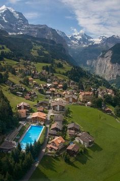 an aerial view of a small village with a pool in the foreground and mountains in the background