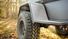 an off road vehicle parked in the woods with leaves on the ground and trees behind it