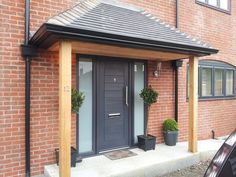 a grey front door with two potted plants on the steps and a black awning over it