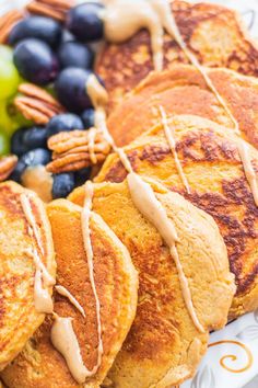 pancakes with maple syrup and blueberries on a white plate next to pecans, grapes and nuts