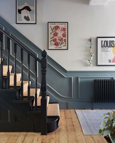 a staircase with pictures on the wall and wooden flooring next to it, in front of a blue painted stair case