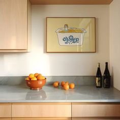 a bowl of oranges sitting on top of a kitchen counter next to bottles of wine