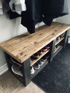 a wooden bench with several pairs of shoes on it in front of a coat rack