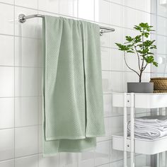 a green towel hanging on the side of a white tiled wall next to a potted plant