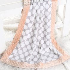 a blanket that is laying on top of a white chair with polka dot print and pink trim