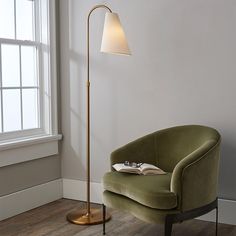 a green chair sitting next to a lamp on top of a hard wood floor in front of a window