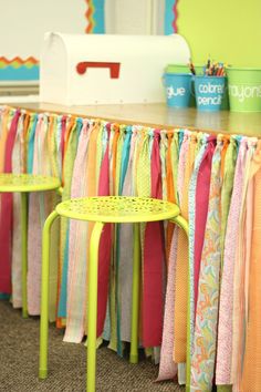 a row of colorful ribbons hanging on a wall next to a table with two stools