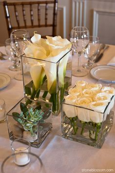 two vases filled with flowers on top of a table next to wine glasses and silverware