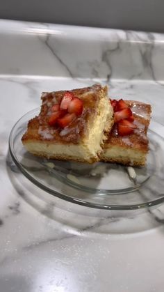 two pieces of cake sitting on top of a glass plate next to a bowl of strawberries