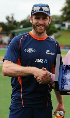 two men shaking hands on a field with an orange and blue uniform holding a bottle