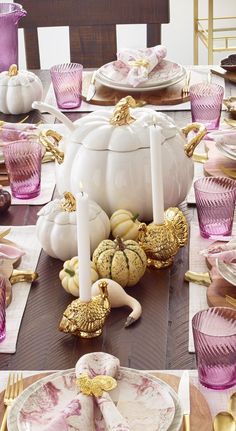 the table is set with pink and white dishes, gold candlesticks, and pumpkins