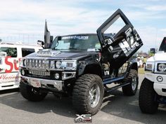 a black hummer truck parked in a parking lot next to other white pickup trucks