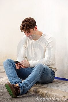 a young man sitting on the ground looking at his cell phone while he is waiting for something to happen