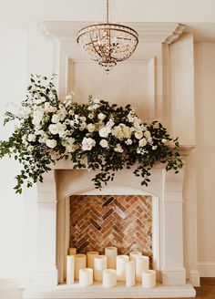 a fireplace with candles and flowers on it in front of a chandelier filled with white roses