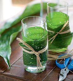 two glasses filled with green liquid sitting on top of a wooden table next to scissors