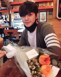 a young man sitting at a table with flowers in a bag on top of it