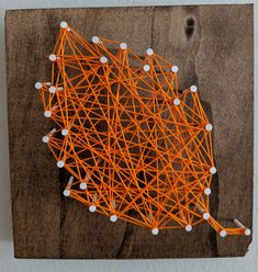 an orange and white string art piece sitting on top of a wooden board with pins stuck to it