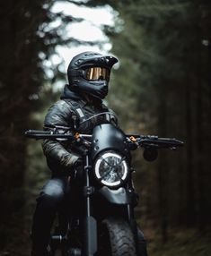 a man riding on the back of a motorcycle down a forest road