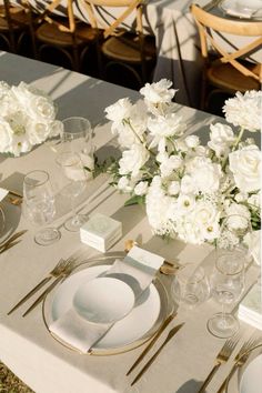 the table is set with white flowers and silverware