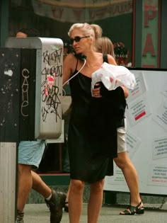 a woman walking down the street while talking on a cell phone and holding onto a man's arm