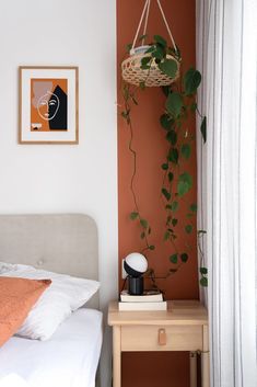 a bedroom with a bed, nightstand and plant hanging on the wall next to it