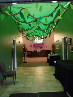 an empty room with tables and chairs in the center is decorated with green leaves hanging from the ceiling