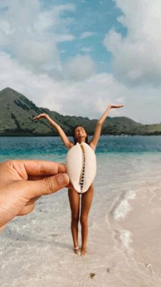 a person holding up a white surfboard on the beach with mountains in the background