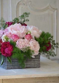 a basket filled with pink and red flowers on top of a white table next to a wall