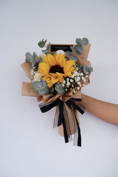 a sunflower and succulent bouquet is wrapped in brown paper with black ribbon