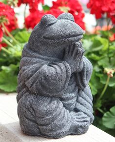 a buddha statue sitting on top of a wooden bench in front of red and white flowers