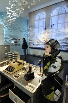 a woman standing in front of a desk with an old typewriter and telephone on it