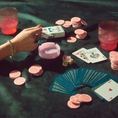 a person is playing cards and other items on a table with pink cups, dices, and candles