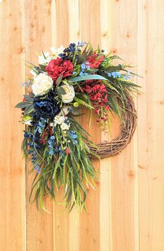 a wreath with red, white and blue flowers hanging on a wooden fence