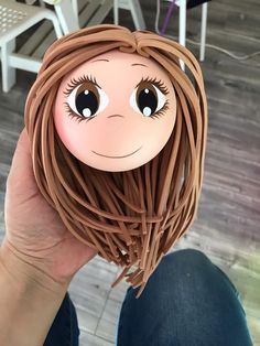 a person holding up a cardboard doll with long brown hair and big eyes on it's face