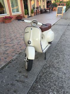 a white scooter parked on the side of a street next to a sidewalk