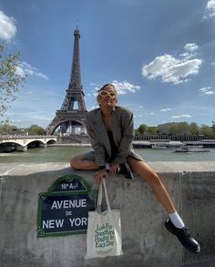 a woman sitting on the edge of a wall with a shopping bag in front of the eiffel tower