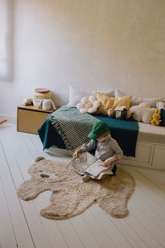 a young child sitting on the floor reading a book in a bedroom with stuffed animals