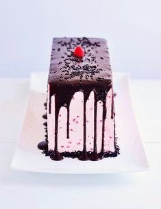 a piece of chocolate cake with pink icing and sprinkles on a white plate