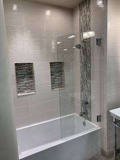 a bathroom with a glass shower door and white bathtub next to a sink area