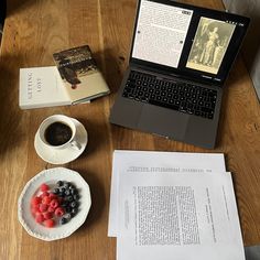 an open laptop computer sitting on top of a wooden table next to a bowl of fruit