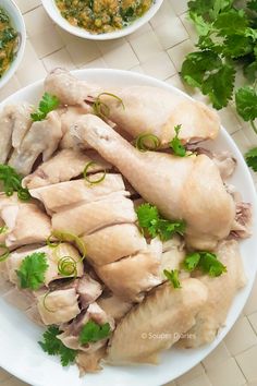 a white plate topped with sliced chicken next to bowls of soup and cilantro