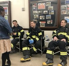 four firemen sitting in chairs talking to each other and one man standing next to them