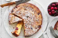 a cake on a plate with some cherries next to it and a knife and fork