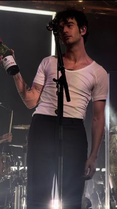 a man holding a wine bottle in his hand while standing next to a drum set